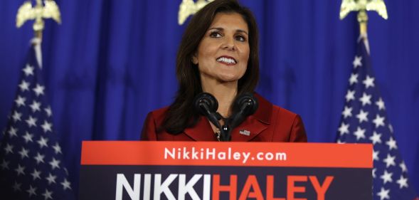 Republican presidential nomination candidate Nikki Haley smiles while wearing a red outfit as she stands in front of podium with her name on it
