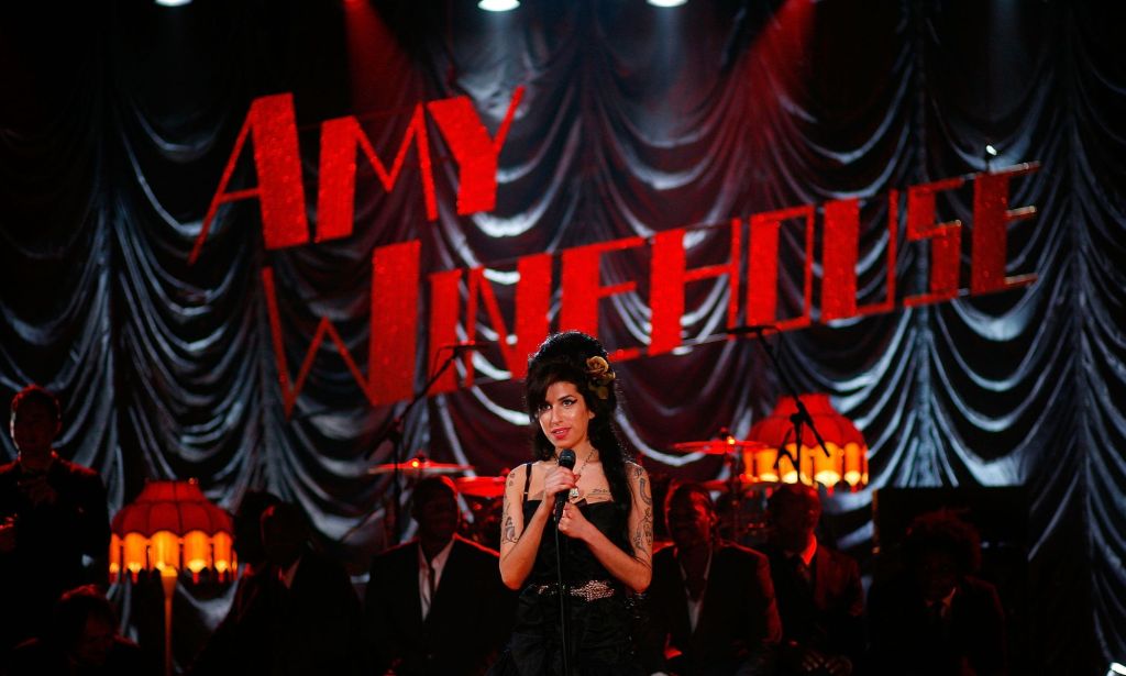 Amy Winehouse performs in front of a red sign that says Amy Winehouse.