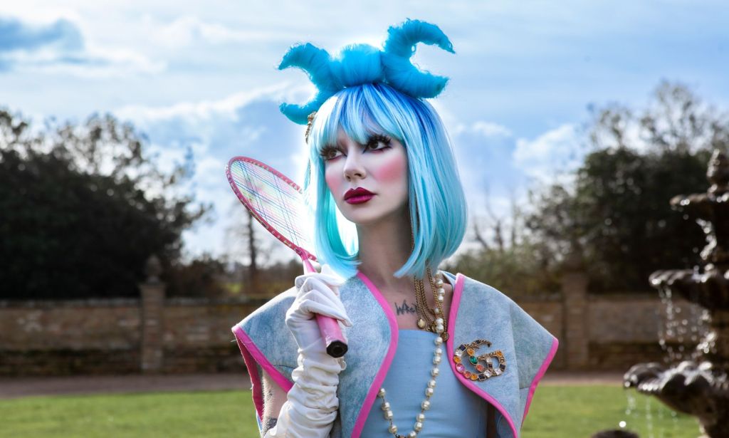Bambie Thug in a blue wig holding a pink tennis racket.