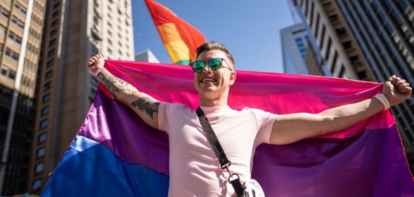 Stock image of a man holding a bi flag behind him to illustrate Bi Pride UK