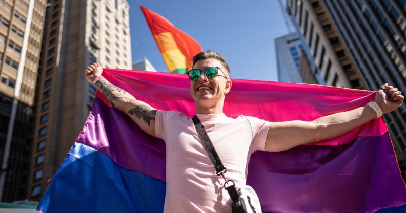 Stock image of a man holding a bi flag behind him to illustrate Bi Pride UK