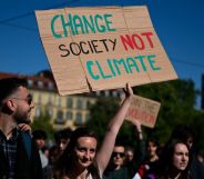Person at a climate change march holds a sign reading "change society not climate"