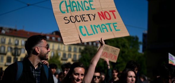 Person at a climate change march holds a sign reading "change society not climate"