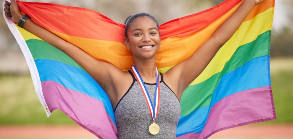 A female-presenting athlete with a medal holding a rainbow flag