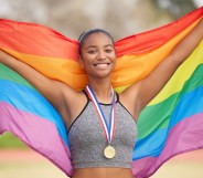 A female-presenting athlete with a medal holding a rainbow flag