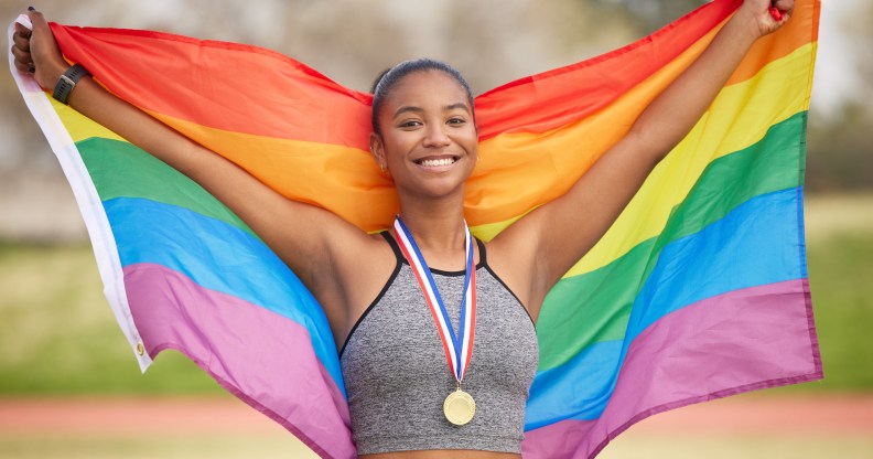 A female-presenting athlete with a medal holding a rainbow flag