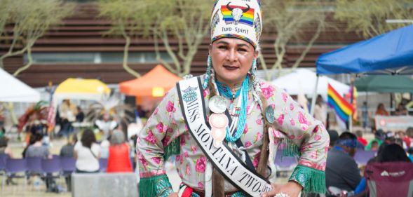 A Two Spirit person dances at an event in elaborate traditional dress