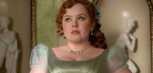 Nicola Coughlan wears a green dress and ginger hair in Bridgerton season three still. She is looking skyward and solemn.