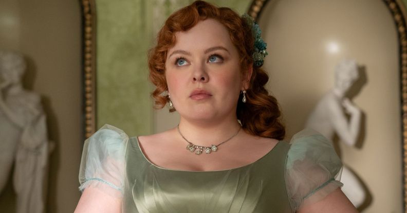 Nicola Coughlan wears a green dress and ginger hair in Bridgerton season three still. She is looking skyward and solemn.