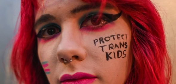 A close up of a trans activist with the words "protect trans kids" written on their face.