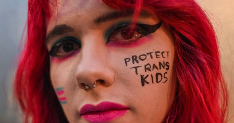 A close up of a trans activist with the words "protect trans kids" written on their face.