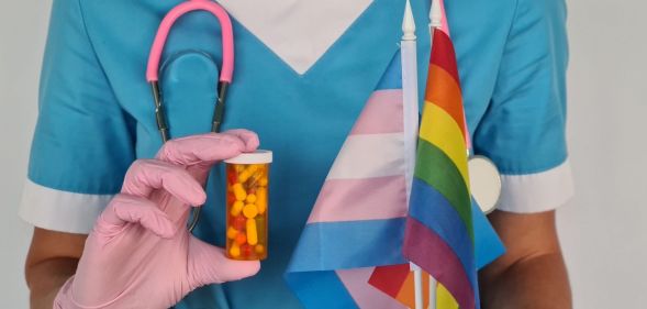 A doctor holding a trans flag, a Pride flag, and a capsule of pills.