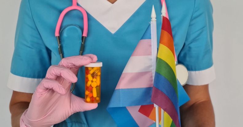 A doctor holding a trans flag, a Pride flag, and a capsule of pills.