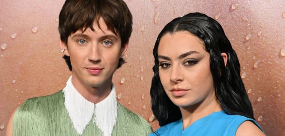 Troye Sivan in a frilly green top with a white collar standing next to Charli XCX who is wearing a blue armless dress. They are stood against a sweaty background.