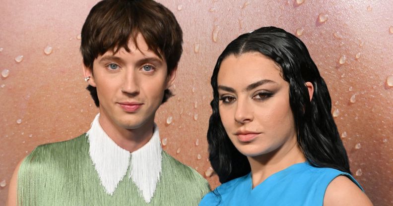 Troye Sivan in a frilly green top with a white collar standing next to Charli XCX who is wearing a blue armless dress. They are stood against a sweaty background.