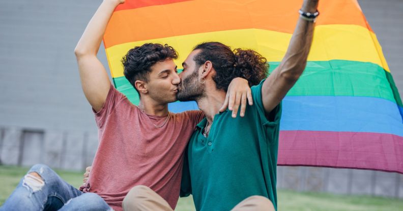 Stock image of two men kissing beneath a Pride flag