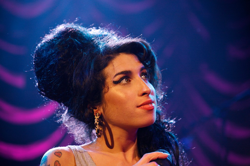 Amy Winehouse looks off to the left while holding a microphone.