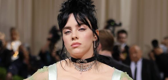 Billie Eilish with black hair done up in a bun, wearing a black choken and a strappy green dress at the 2022 MET Gala.