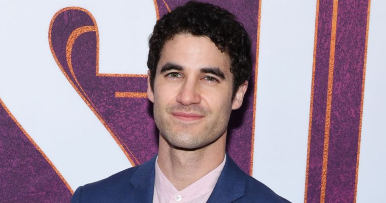 Darren Criss, a non-LGBTQ+ actor who got famous for playing queer roles, wears a blue blazer and pink shirt while smiling at the camera.