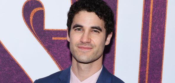 Darren Criss, a non-LGBTQ+ actor who got famous for playing queer roles, wears a blue blazer and pink shirt while smiling at the camera.