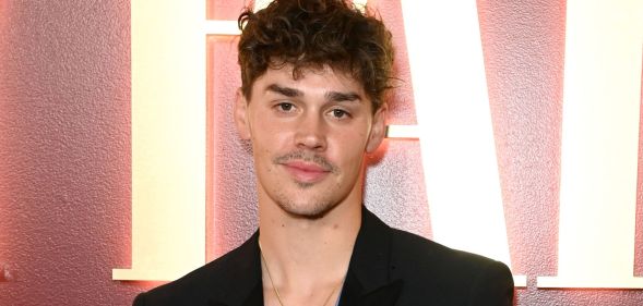 Noach Beck wears a black blazer and blue and white top with a necklace at a Vanity Fair event.