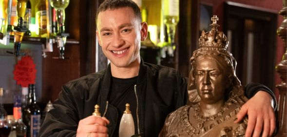 Olly Alexander smiles as he stands behind the bar in EastEnders pub The Queen Vic, pulling a pint.