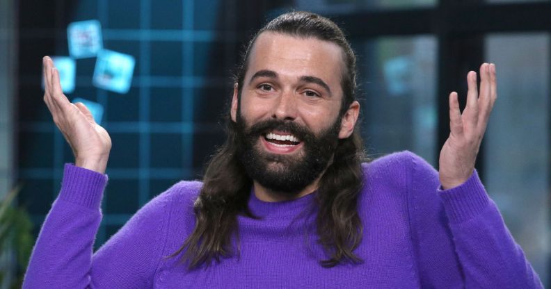Jonathan Van Ness smiles and shrugs with their hands in the air.
