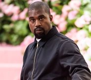 Rapper Ye, formerly known as Kanye West, wears a black tracksuit jacket as he stands in front of a green and pink background
