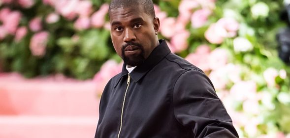 Rapper Ye, formerly known as Kanye West, wears a black tracksuit jacket as he stands in front of a green and pink background