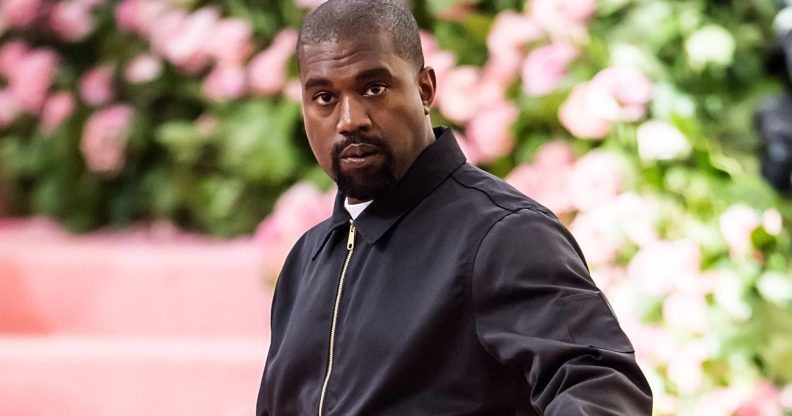 Rapper Ye, formerly known as Kanye West, wears a black tracksuit jacket as he stands in front of a green and pink background