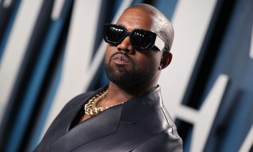 Rapper Ye, formerly known as Kanye West, wears a dark suit jacket, gold necklace and dark sunglasses
