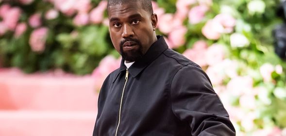 Rapper Ye, formerly known as Kanye West, wears a black tracksuit jacket as he stands in front of a green and pink background