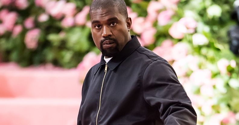 Rapper Ye, formerly known as Kanye West, wears a black tracksuit jacket as he stands in front of a green and pink background