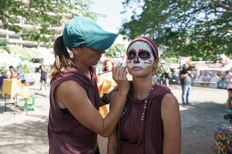 Photo shows lesbian couple Yvonne Chavez and Melissa Main applying face paint on The Amazing Race