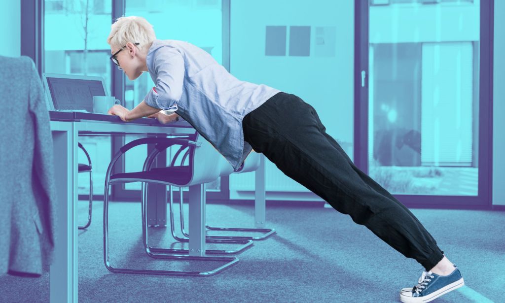 This is an image of a person doing a push up on a desk in an office.
