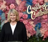 Marsha Stewart in front of a multicoloured floral display that, to be honest, we chose as it kind of looked like the colours of the trans flag.