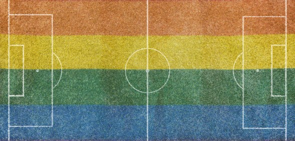 Aerial view of a grass soccer field without people and with painted white lines, with the lgtb rainbow flag painted on the grass.