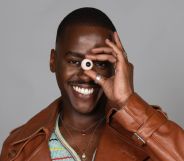 Ncuti Gatwa smiles while holding a fake eye up to his face.