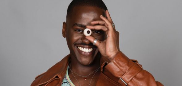 Ncuti Gatwa smiles while holding a fake eye up to his face.