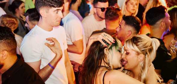 man looking on as two women kiss in popworld