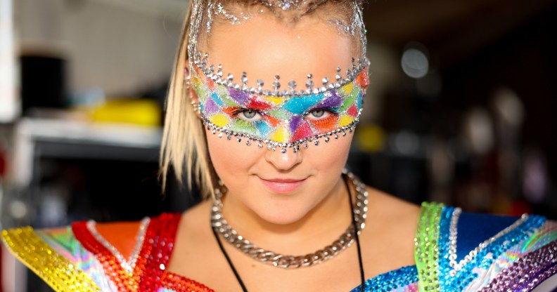 JoJo Siwa dressed in a rainbow concert outfit and rainbow makeup band across her eyes.