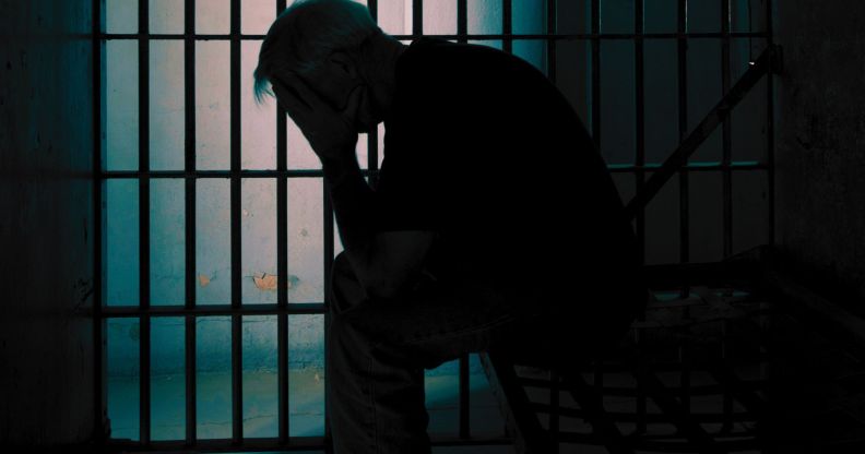 A person holding their head in their hands in a prison cell.