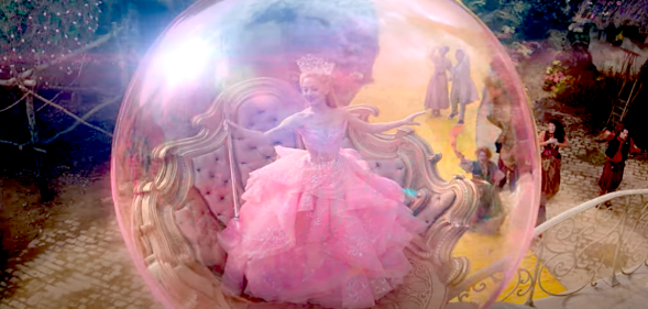 Photo shows Ariana Grande as Glinda The Good Witch floating in a pink bubble wearing a pink dress and holding a wand