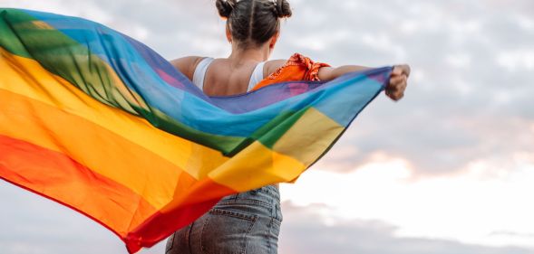Girl stands holding an LGBTQ+ flag behind her back