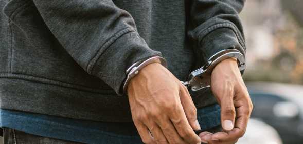 Under arrest, a man's hands with clenched fists are handcuffed behind him.