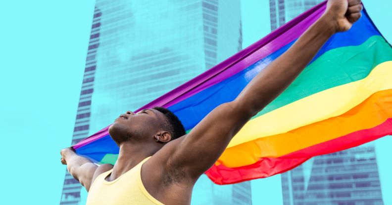 This is an image of a Black man holding a Pride flag in front of an office building