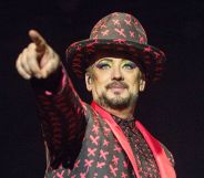 Boy george performing in a red and black patterned outfit and hat