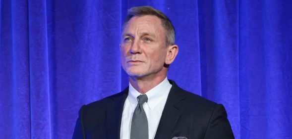 Daniel Craig in a suit and tie against a blue curtain