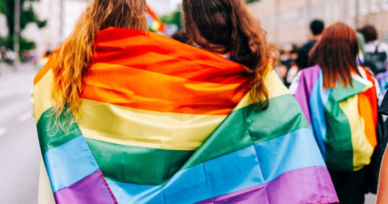 Two women wearing an LGBTQ+ Pride flag