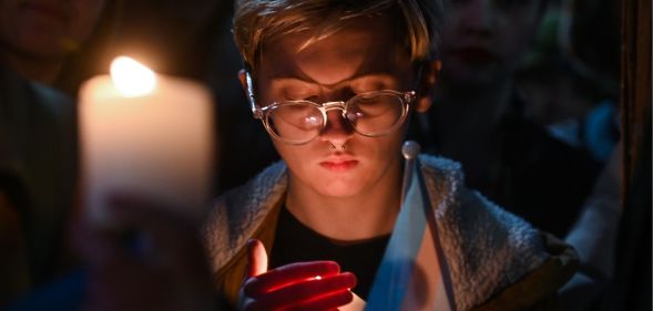 A person holds a candle and a trans flag at the vigil for murdered schoolgirl Brianna Ghey